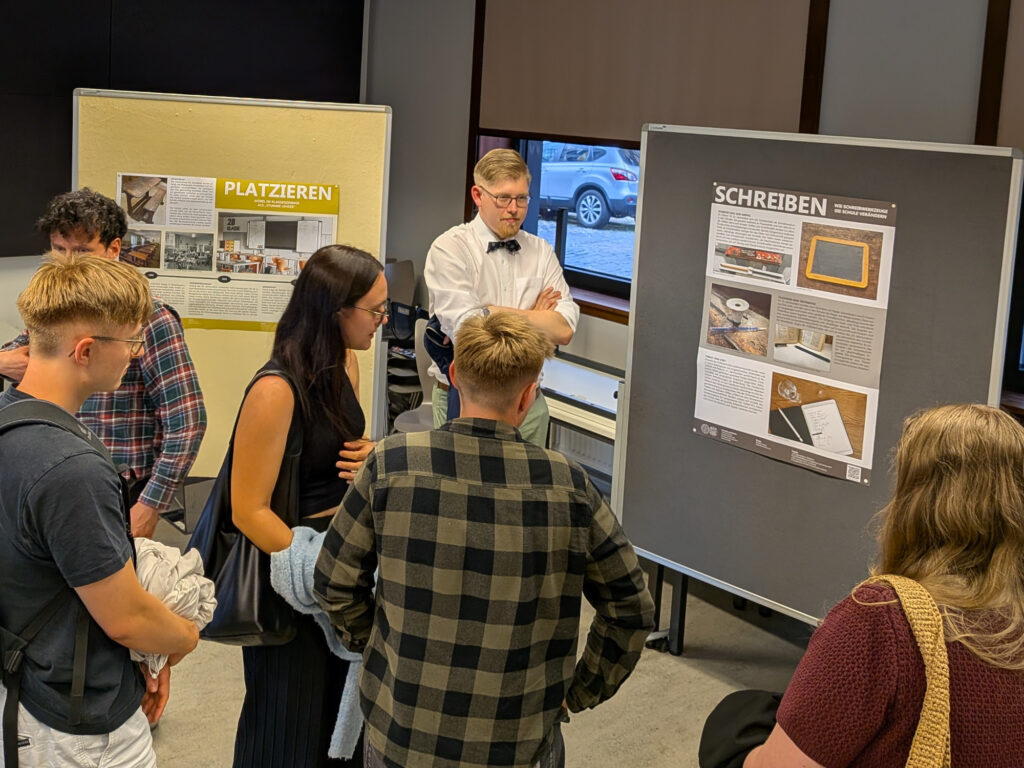 Ausstellung "Schulgeschichte in Objekten" auf der Lange Nacht der Wissenschaften 2026 in Halle Ausstellung "Schulgeschichte in Objekten" auf der Lange Nacht der Wissenschaften 2026 in Halle, einige Besucher:innen vor Plakaten mit den Titeln "Platzieren" und "Schreiben"